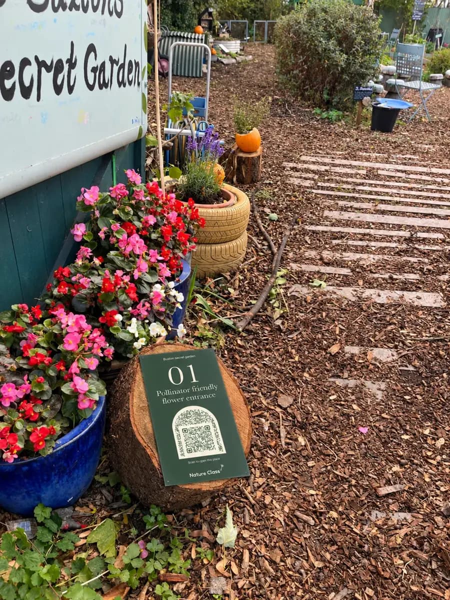 Sign 01 on a log round beside pots of red and pink flowers